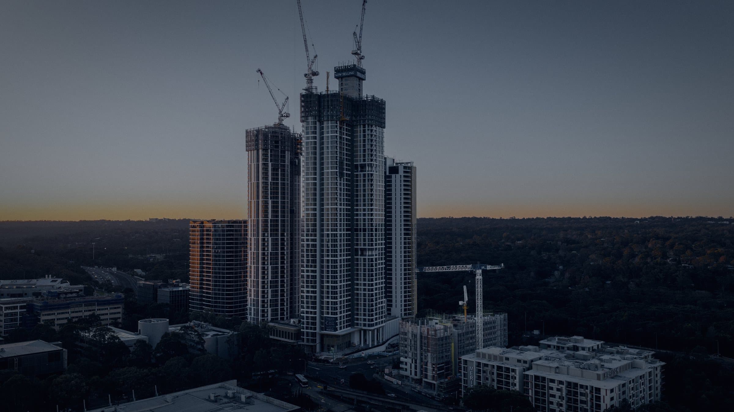 Residential towers under construction at dusk, tower cranes on their cores.